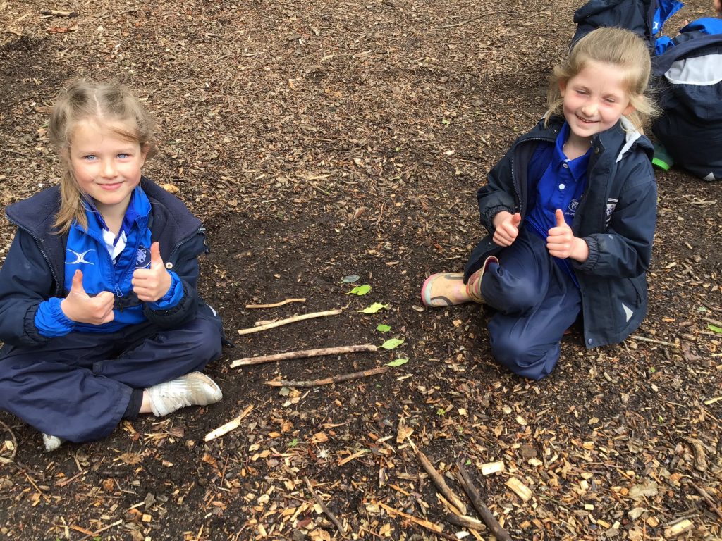 2 girls with their thumbs up in the forest