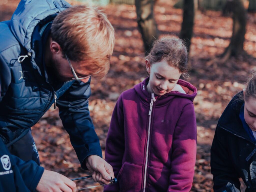 Teacher supports prep school children in outdoor learning using tools
